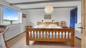 A bedroom with a wooden bed, a window with a view, a bedside table with a lamp, and a chair.