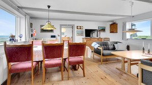 A spacious living area with a dining table, red upholstered chairs, a sofa, and a television.