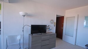 Une pièce avec un téléviseur posé sur un meuble en bois, un lampadaire, une porte et un élément de décoration murale.