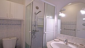 Une salle de bain dotée d’une douche à parois de verre, de toilettes, d’un lavabo avec un plan de toilette en marbre et d’un grand miroir.
