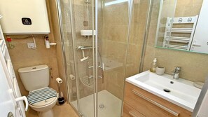 A modern bathroom with a glass-enclosed shower, a toilet with a striped seat, and a white sink with a mirror above it. - Studio 2 people – Sea view – Air conditioning – WiFi – Downtown – Near the beach –... (STE MAXIME)