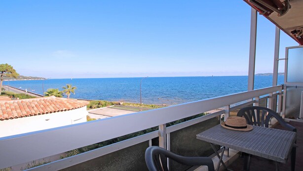 Un balcon avec vue sur la mer, une table avec un chapeau et une chaise.
