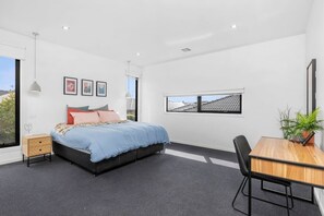 Quarto com cama, mesa de cabeceira e escrivaninha com cadeira.