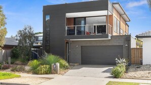 Ett modernt hus i två våningar med garage, balkong och en välskött trädgård.