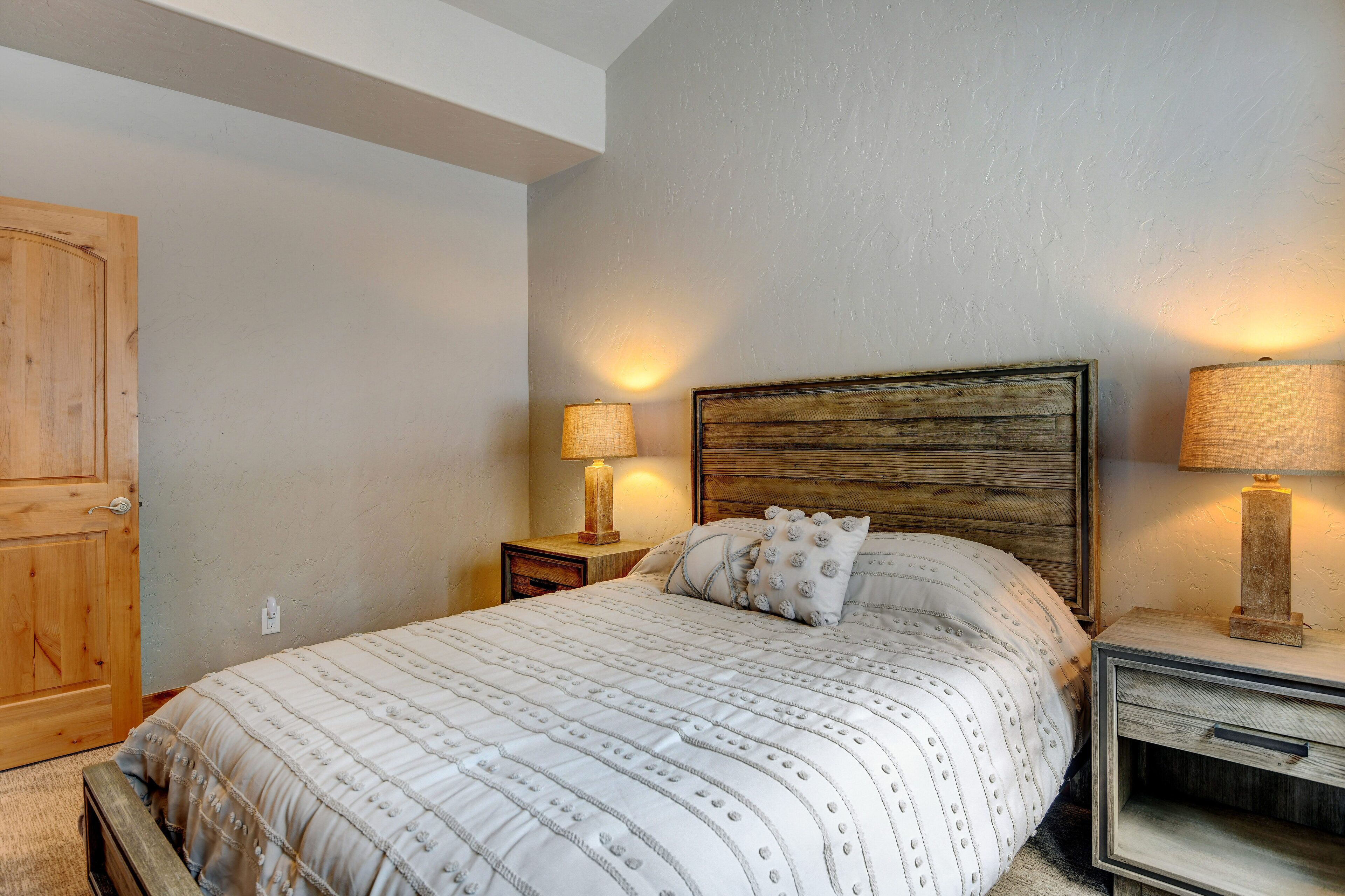 Un dormitorio con una cama grande, cabecera de madera, dos mesitas de noche con lámparas y un armario de madera.