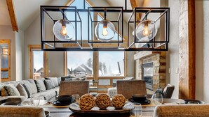 Un comedor moderno con una mesa de madera preparada para cuatro personas, una chimenea de piedra y un amplio ventanal con vistas a un paisaje nevado.