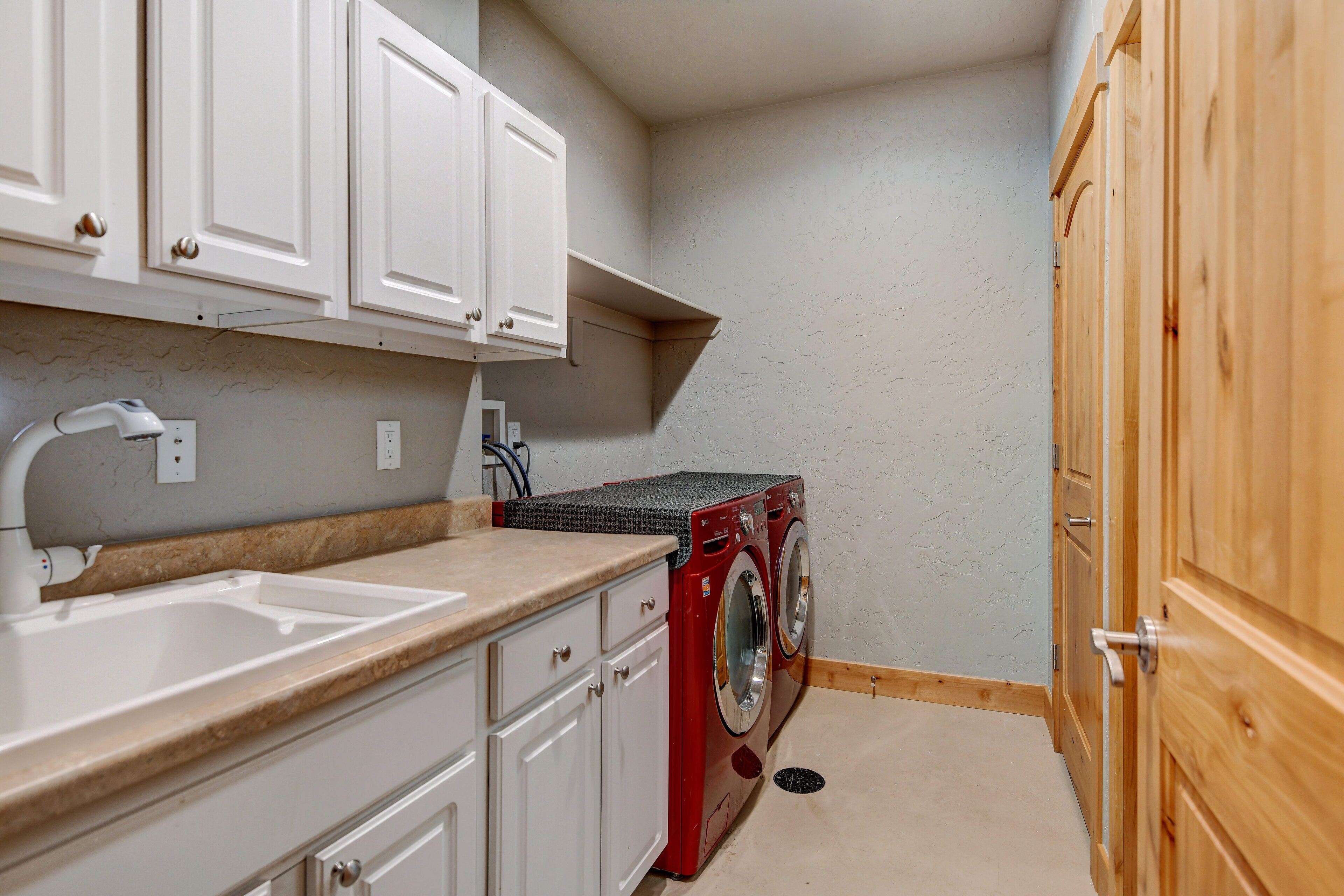 A compact kitchen with white cabinets, a sink, a washing machine, and a wooden door.