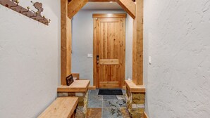 Una puerta de madera con un felpudo negro, un banco a la izquierda y un suelo de baldosas de piedra.