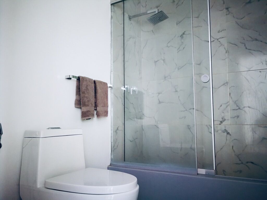 A bathroom with a white toilet, a glass shower enclosure, and a marble-patterned wall.