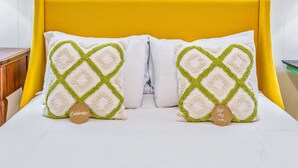 A bed with a yellow headboard, two pillows with a diamond pattern, and a round tag with text.