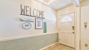 A hallway with a 'WELCOME' sign, a framed picture, a decorative plate, and a door with a window.