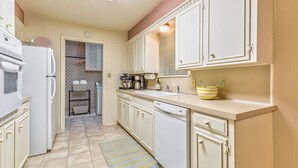 A kitchen with white cabinets, a refrigerator, a coffee maker, and a striped rug.