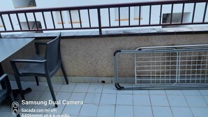 Un balcone con tavolo e sedie, ringhiera in metallo e un edificio sullo sfondo.