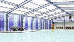 Una piscina interior con techos altos y ventanas amplias.