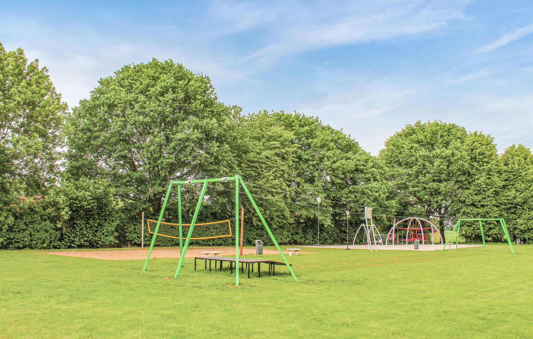 Un parc avec de l’herbe verte, des arbres et des équipements de jeux pour enfants, notamment des balançoires et une structure d’escalade.