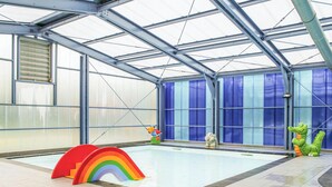 Una piscina interior con techo de vidrio, un trampolín con forma de arcoíris y esculturas de animales de caricatura.