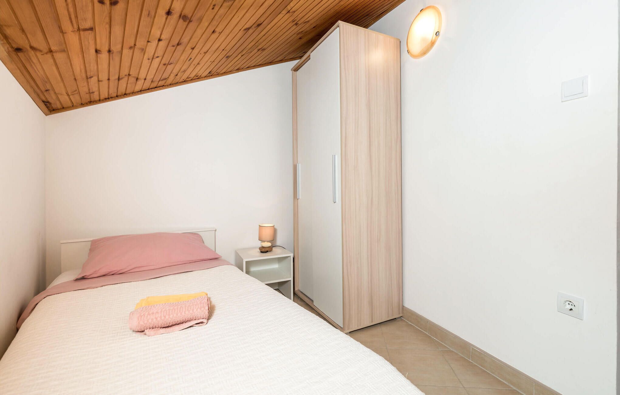 Une chambre à coucher comprenant un lit, une table de chevet, une lampe, une armoire et un luminaire au plafond.