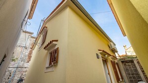 A narrow street with a building featuring a small window with wooden shutters, a visible air conditioning unit, and a door with a metal grid. - Gorgeous home in Susak with WiFi (Susak)