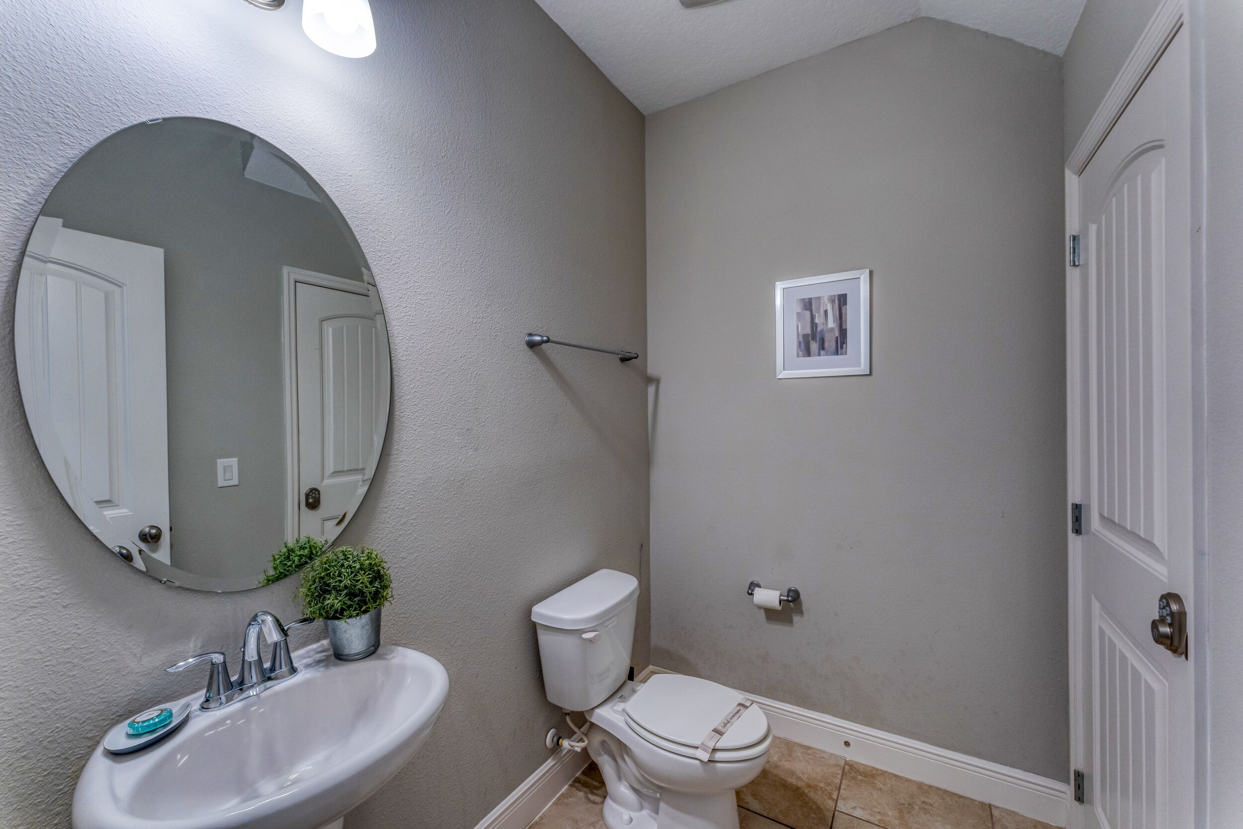 A bathroom with a round mirror, a sink, a toilet, and a small framed picture on the wall.