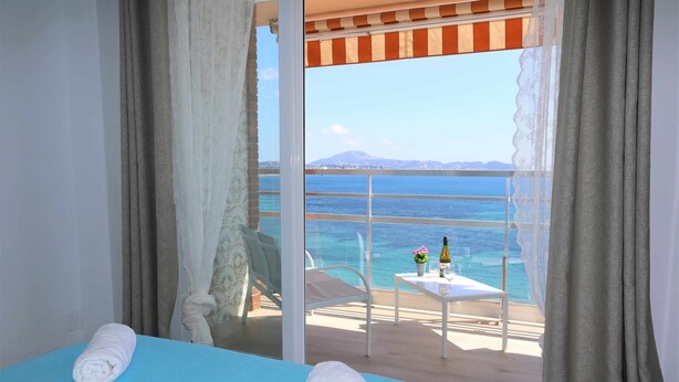 A room with a bed, a table with a bottle and flowers, and a view of the sea and mountains. - 11F 2 Dormitorios con Vistas al mar (Calp)