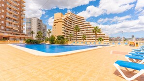 A swimming pool with sun loungers, surrounded by palm trees and a high-rise building with balconies. - 11F 2 Dormitorios con Vistas al mar (Calp)