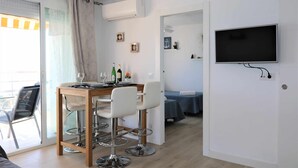 A modern room with a dining area, a TV mounted on the wall, and a balcony with a sliding door. - 11F 2 Dormitorios con Vistas al mar (Calp)
