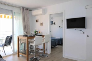 Una habitación moderna con comedor, televisor en la pared y balcón con puerta corredera.