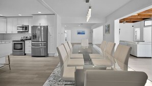 A modern kitchen with stainless steel appliances, a dining area with a glass table and chairs, and a view of the living room. - 2260 Managed By Brampton Park (Pompano Beach)