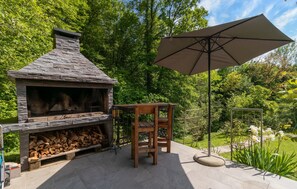 Een buitenhaard van natuursteen met schoorsteen, een houten tafel en een parasol.