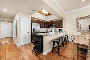 Une cuisine moderne avec des meubles en bois, un réfrigérateur en acier inoxydable, un four à micro-ondes et un grand îlot central doté de tabourets de bar.