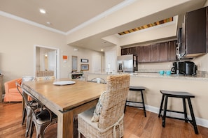 Un comedor con mesa y sillas de madera, una cocina con armarios oscuros y encimera, y un pasillo que conduce a otra habitación.