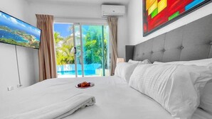 Habitación de hotel con cama, televisión de pantalla plana, un cuadro y vista a una piscina y follaje.