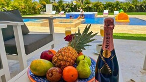 Et tropisk resorthotell med pool, liggestole og et bord med frugt og en champagneflaske.