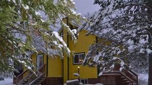 A yellow building with a staircase leading to a porch, surrounded by snow-covered trees. - La Maison jaune: Spa, comfort, wifi (Chute-Saint-Philippe)
