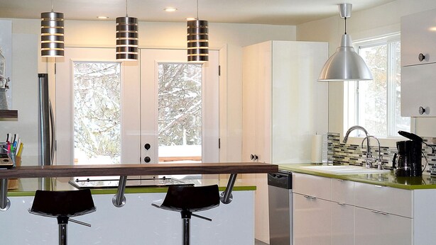 A modern kitchen with white cabinets, a green countertop, and a stainless steel sink. There are two bar stools and three pendant lights. - La Maison jaune: Spa, comfort, wifi (Chute-Saint-Philippe)