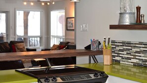 A modern kitchen with a green countertop, stainless steel appliances, and a hanging light fixture. - La Maison jaune: Spa, comfort, wifi (Chute-Saint-Philippe)