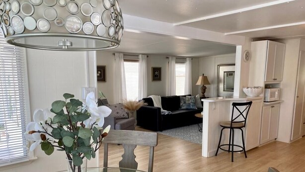 A modern living room with a glass dining table, a sofa, and a kitchen area with cabinets and a microwave. - Cozy retreat, near some of the best Florida beaches! (Bradenton)
