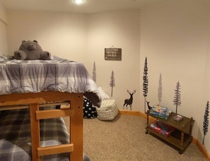 Een kinderkamer met een stapelbed, een knuffel, een welkomstenbord en een klein tafeltje met boeken en speelgoed.