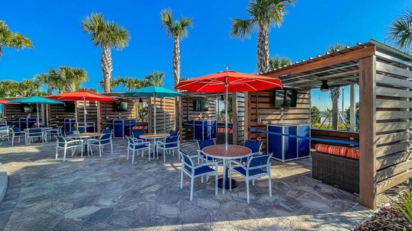 An outdoor patio area with stone flooring, wooden seating, and tables under umbrellas.
