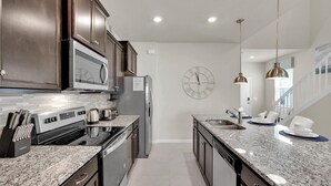 Eine moderne Küche mit dunklen Holzschränken, Edelstahlgeräten, Granit-Arbeitsplatten und einer großen Wanduhr.