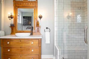 Un baño con tocador de madera, un espejo grande y cabina de ducha con puertas de vidrio.