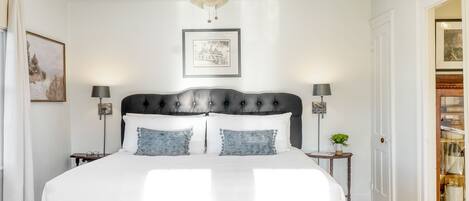 A bedroom with a large bed, a ceiling fan, a framed picture on the wall, and a nightstand with a lamp.