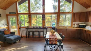 A spacious living room with a large dining table, a sofa, and a kitchen area with wooden cabinets. - Beautiful, private home with fire pit and river access! (Bath)