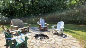 A stone fire pit surrounded by Adirondack chairs in a garden setting. - Beautiful, private home with fire pit and river access! (Bath)