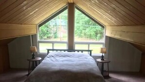 A bedroom with a large bed, two bedside tables, and a window with a view of greenery. - Beautiful, private home with fire pit and river access! (Bath)