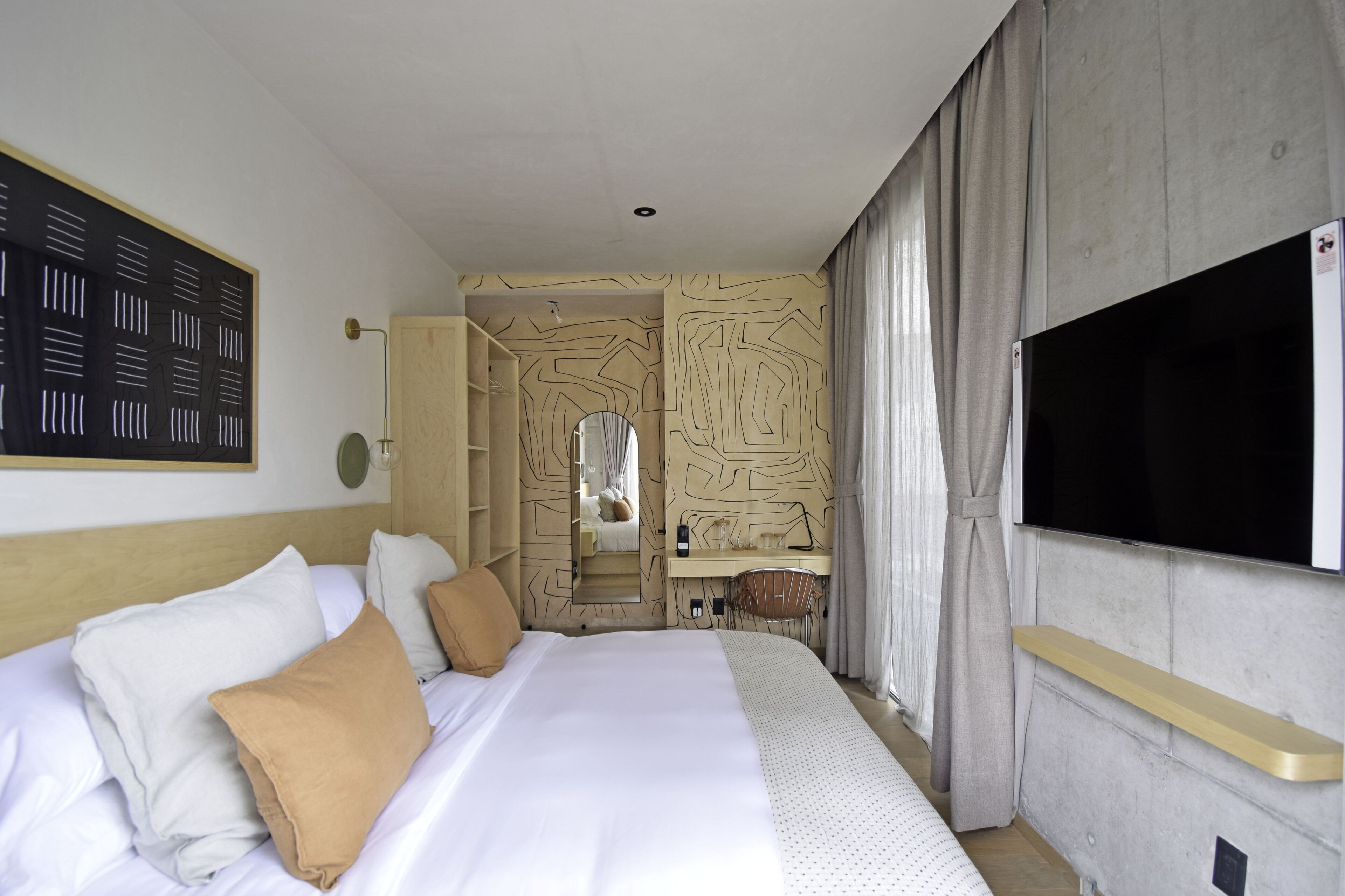 Une chambre d’hôtel avec un grand lit, une télévision, un miroir et une salle de bain visible à travers une porte ouverte.