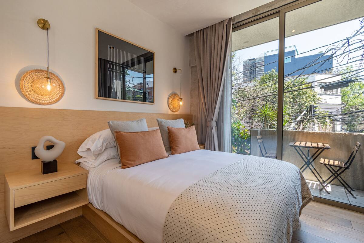 A modern bedroom with a large bed, bedside tables, a mirror, and a view of the outdoors.