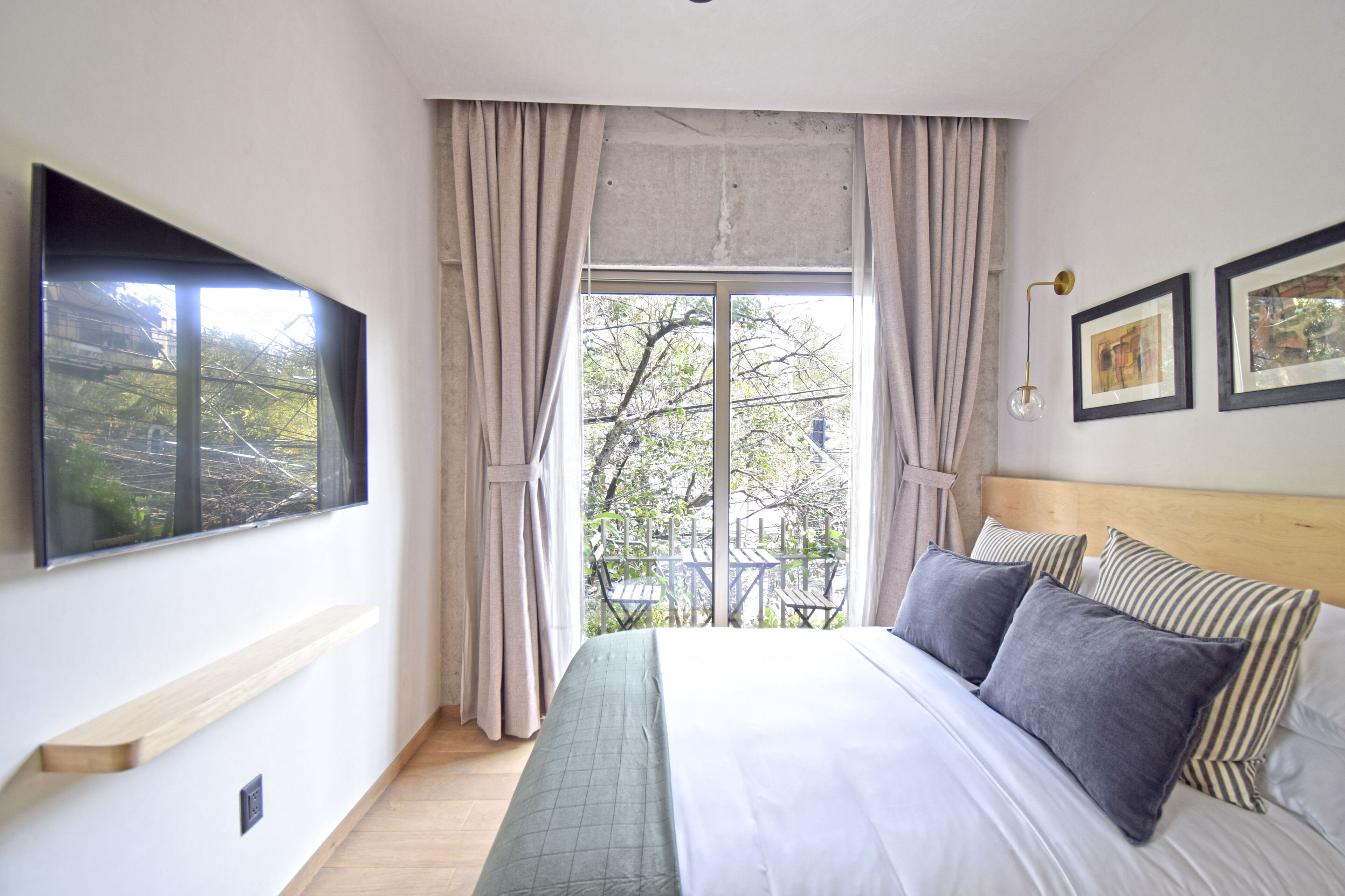 Ein Schlafzimmer mit einem großen Bett, einem an der Wand montierten Fernseher und einem Fenster mit Vorhängen.