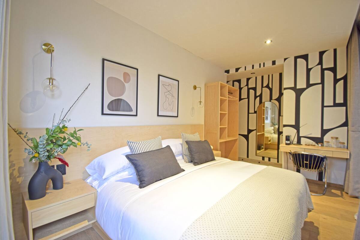 A modern bedroom with a large bed, bedside tables, a wardrobe, and a mirror.