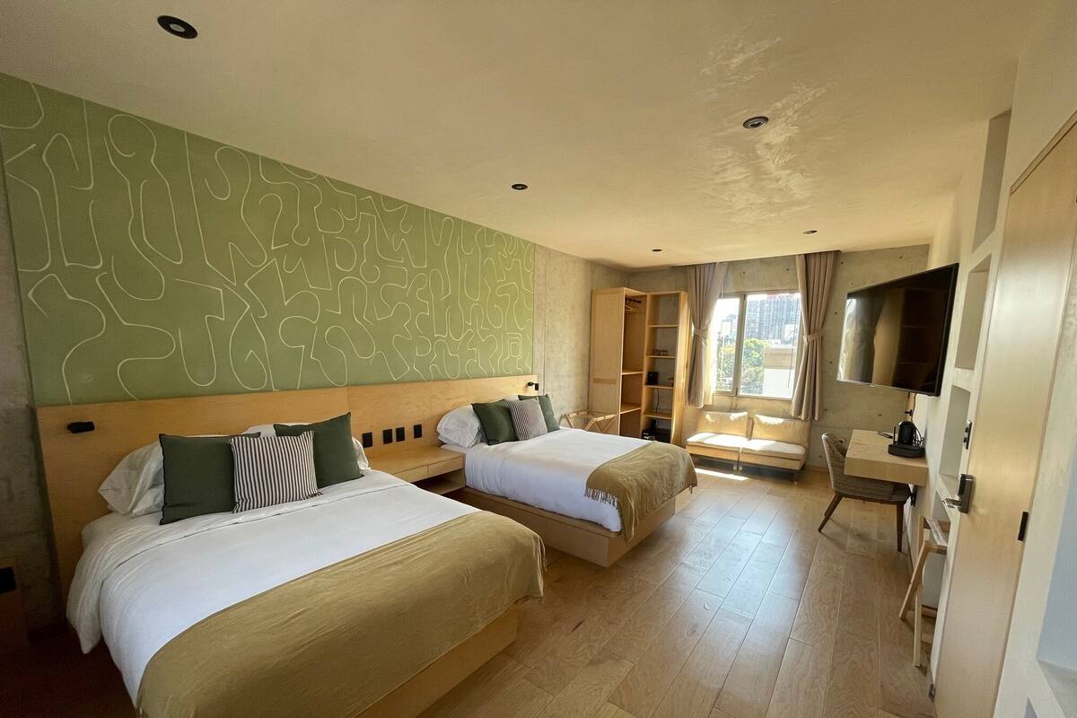 A hotel room with two beds, a desk, a TV, and a window with curtains.